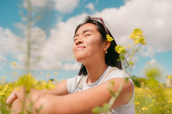 Young woman smiling while sitting in a field of yellow flowers
